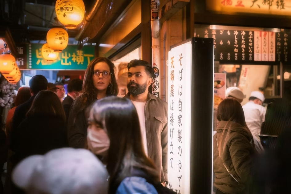 Crowded Japanese street market with lanterns, people, and a sign with Japanese characters.
