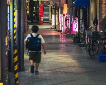 A child walking in a neon-lit alley in Tokyo at night, captured during a street photography workshop.