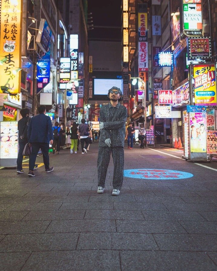 A man wearing a dotted shirt and sunglasses in front of neon signs, captured with an ultra-wide lens.