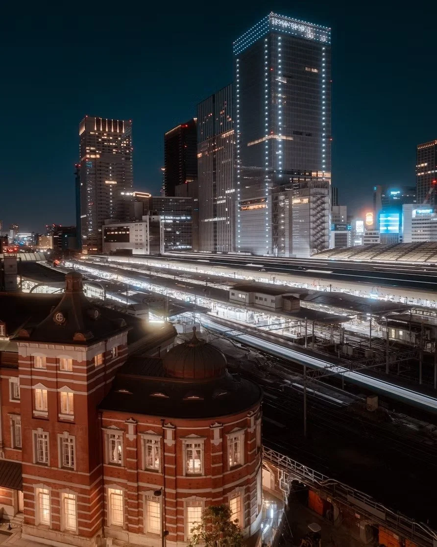 Nighttime cityscape of a modern Tokyo Station area with illuminated skyscrapers and a historical brick building in the foreground.