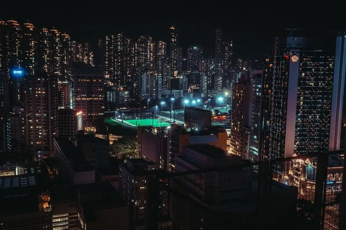 Hong Kong Nighttime city skyline with tall illuminated buildings and tennis courts with bright lights. Shot by Tokyo photographer Deniz Demir.