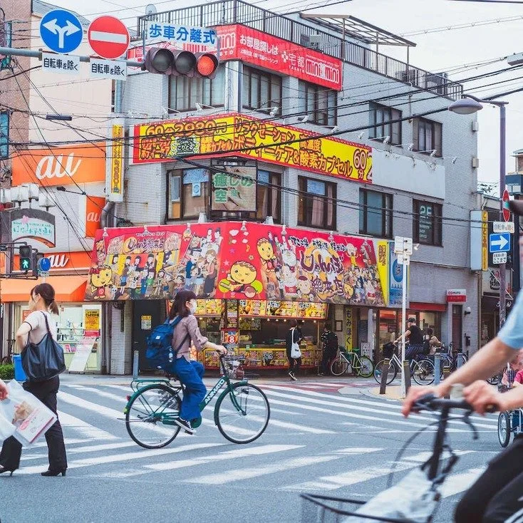People crossing the street in front of a brightly colored building in Osaka during daylight, captured while doing slow travel.