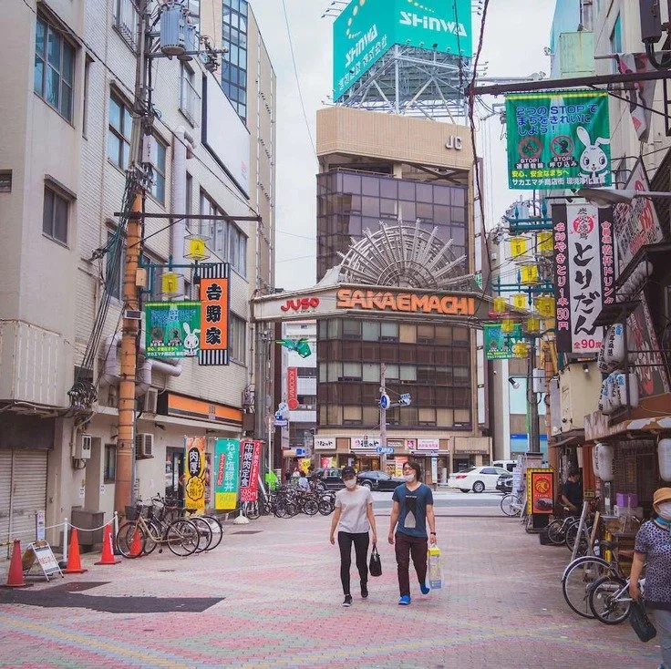 People walking across a colorful street in Osaka, with a prominent sign in the background, during slow travel.