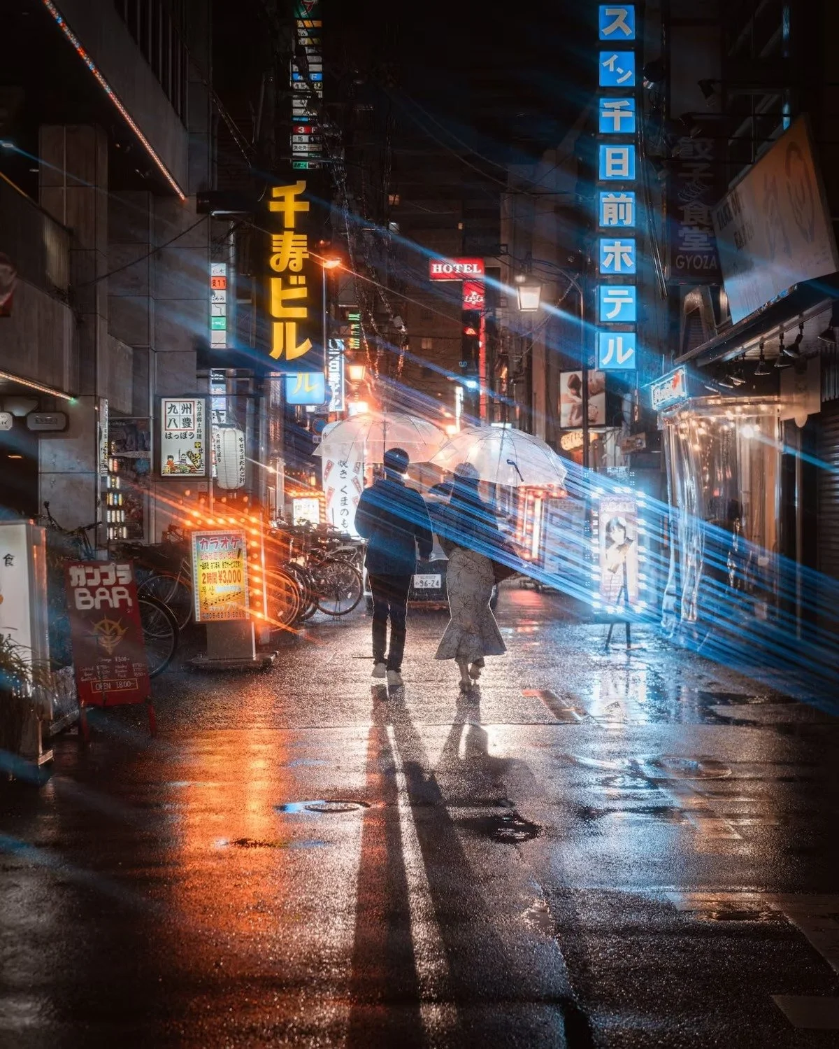 Two people walking on a wet city street at night, holding umbrellas amidst neon signs and rain reflections Osaka.