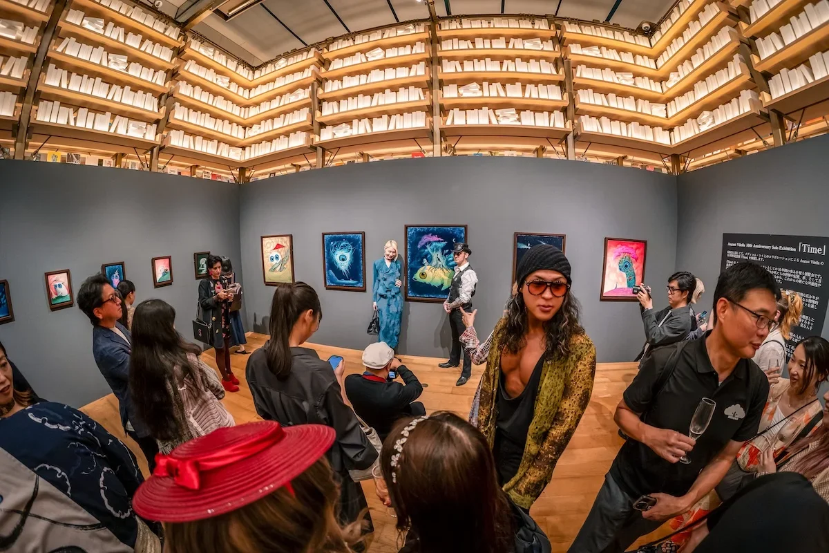August Vilella
---
Wide-angle documentary photograph of contemporary surrealist artist August Vilella's exhibition in Tokyo, Japan, featuring visitors exploring his colourful paintings of fantastical creatures with oversized eyes inside a brightly il