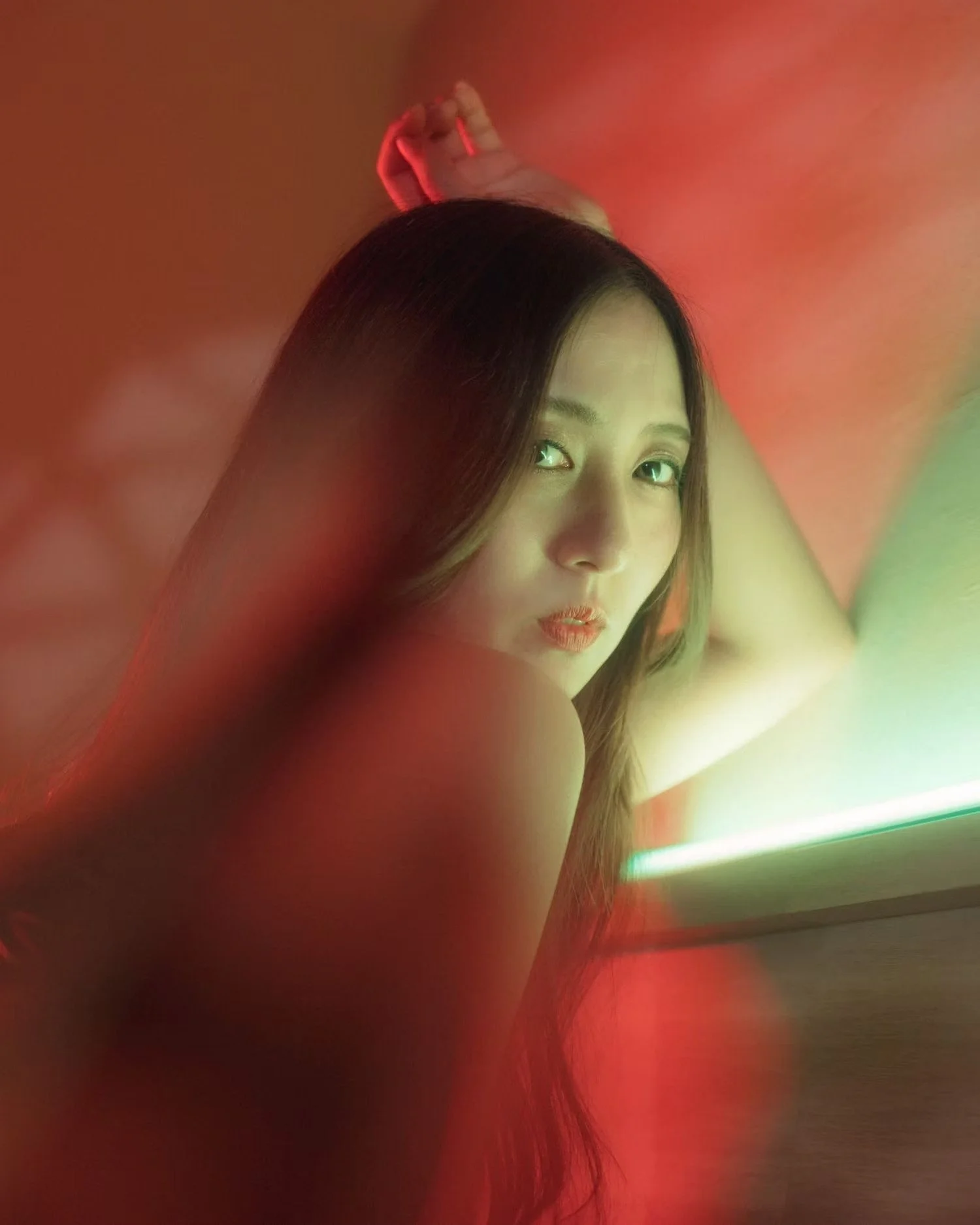 A woman with long dark hair is taking a selfie in a room with predominantly red lighting. She is looking directly at the camera with a slight pout.