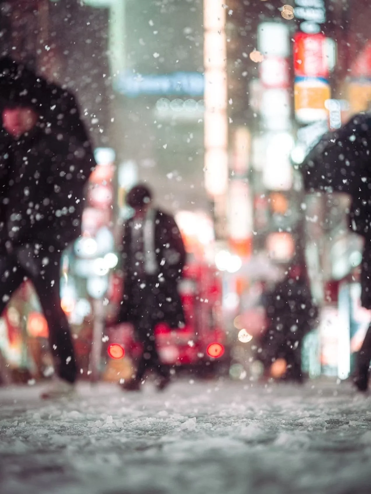 View of a rainy city street seen through a glass window covered with raindrops. Blurred silhouettes of people walking and vehicle taillights glowing in the background.