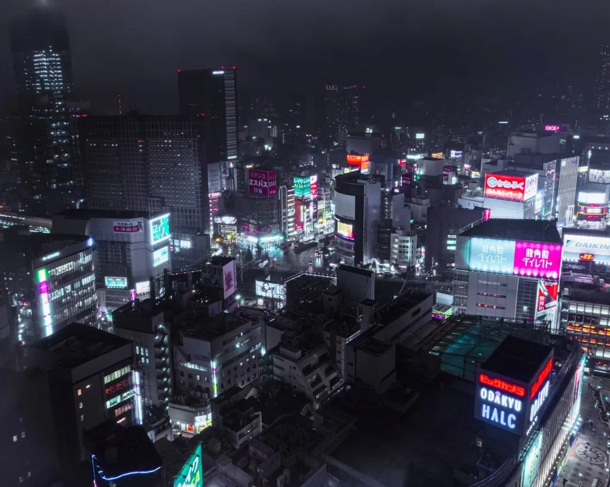 Nighttime cityscape of a busy downtown area with tall buildings illuminated by colorful neon signs and advertisements.