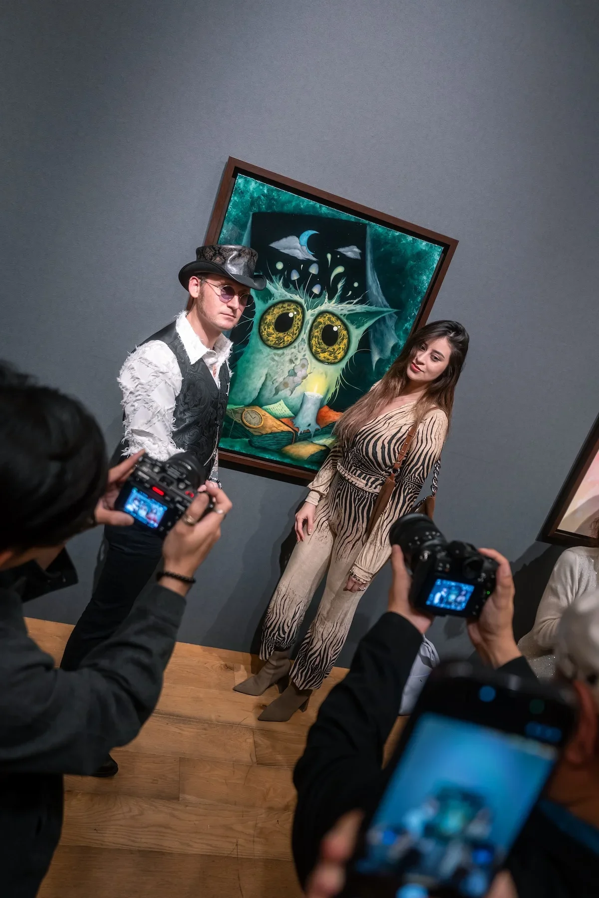 August Vilella
---
Two elegantly dressed guests pose in front of August Vilella's colourful surrealist creature paintings while photographers capture portraits during the contemporary art exhibition.