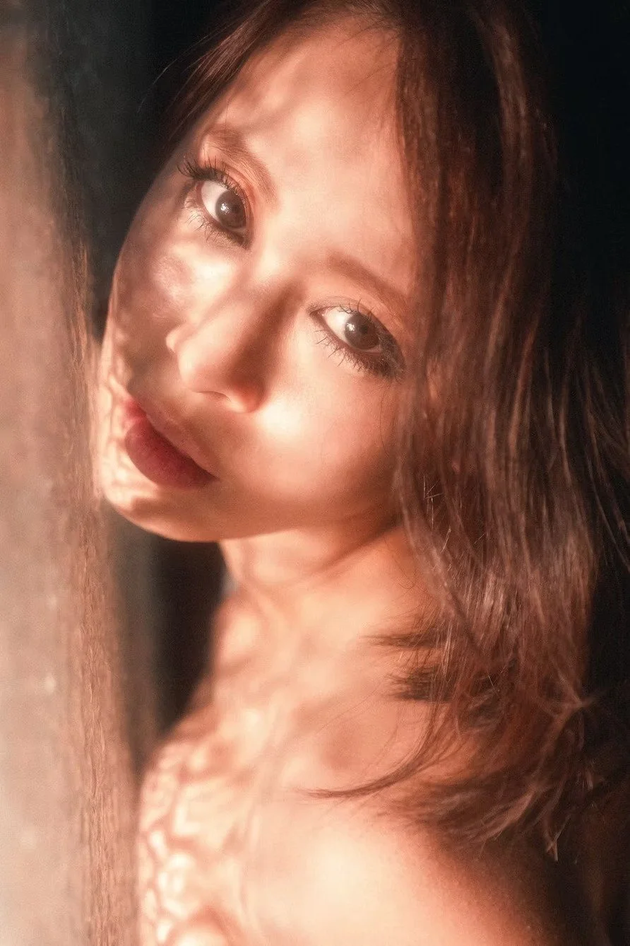 Close-up of a woman with brown hair and brown eyes, lying on her side on a soft surface.