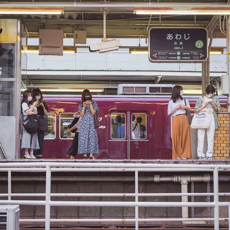 Passengers waiting at an Osaka train station platform, with a train visible in the background, captured during slow travel.