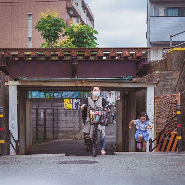 A woman riding a bike while a child runs alongside her near a tunnel in Osaka, captured during a slow travel exploration of the city.