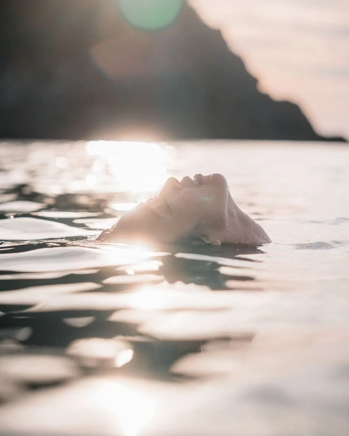 A person floating on their back in a body of water, with the sun setting or rising in the background, creating a serene and peaceful atmosphere in the Japanese islands in summer.