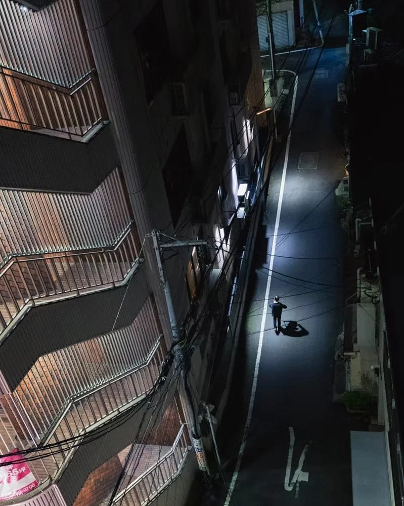 A person walking alone on a dark, empty street at night, illuminated by streetlights.