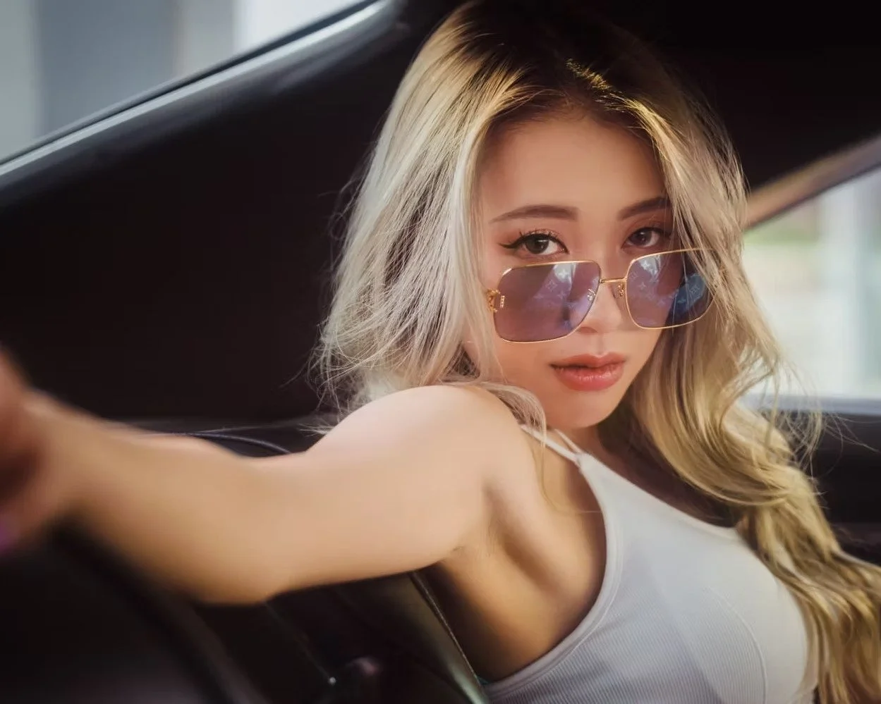 Portrait photography of young woman with blonde hair wearing sunglasses and a white tank top, sitting in a car