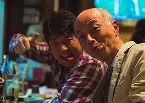 Two men making playful faces while sitting together in a restaurant, enjoying their time in Osaka.