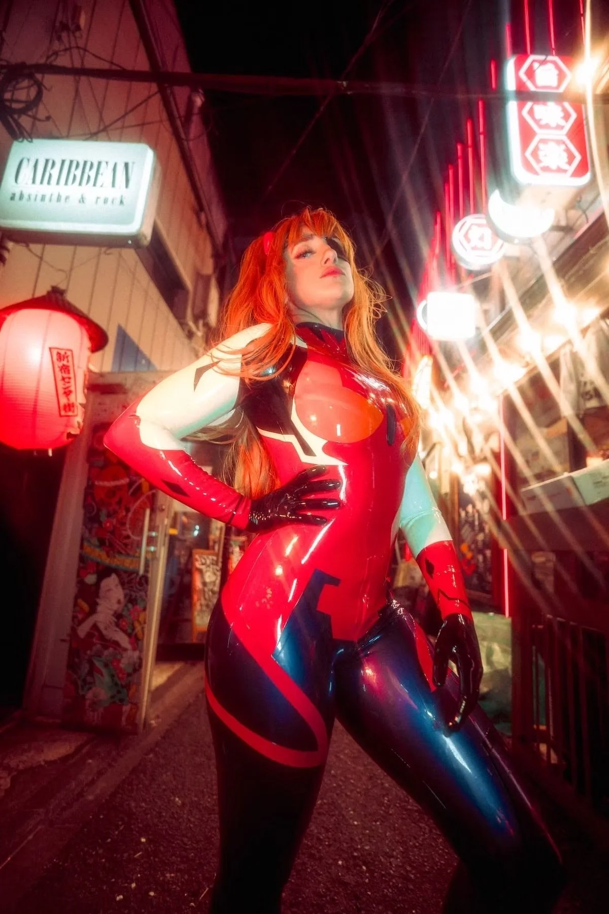 A person cosplaying as Asuka from 'Evangelion' in a red and black bodysuit with orange hair, standing confidently at night in an urban area with neon signs and a red paper lantern. 