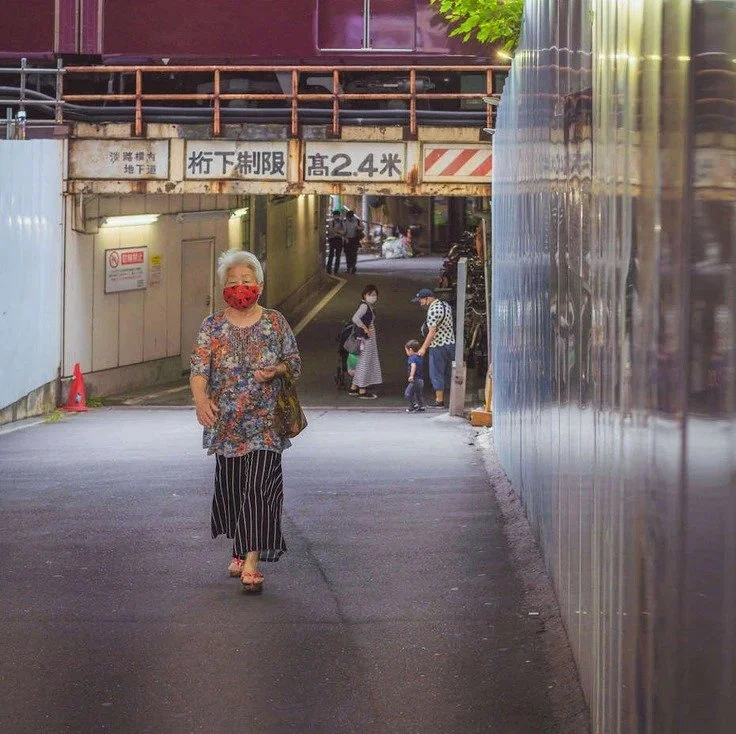 A woman walking through an underpass in Osaka with a train in the background.