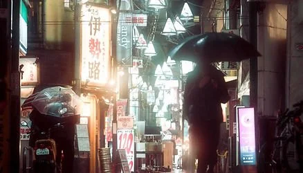 Street scene in Japan at night with people holding umbrellas, neon signs, and illuminated storefronts.