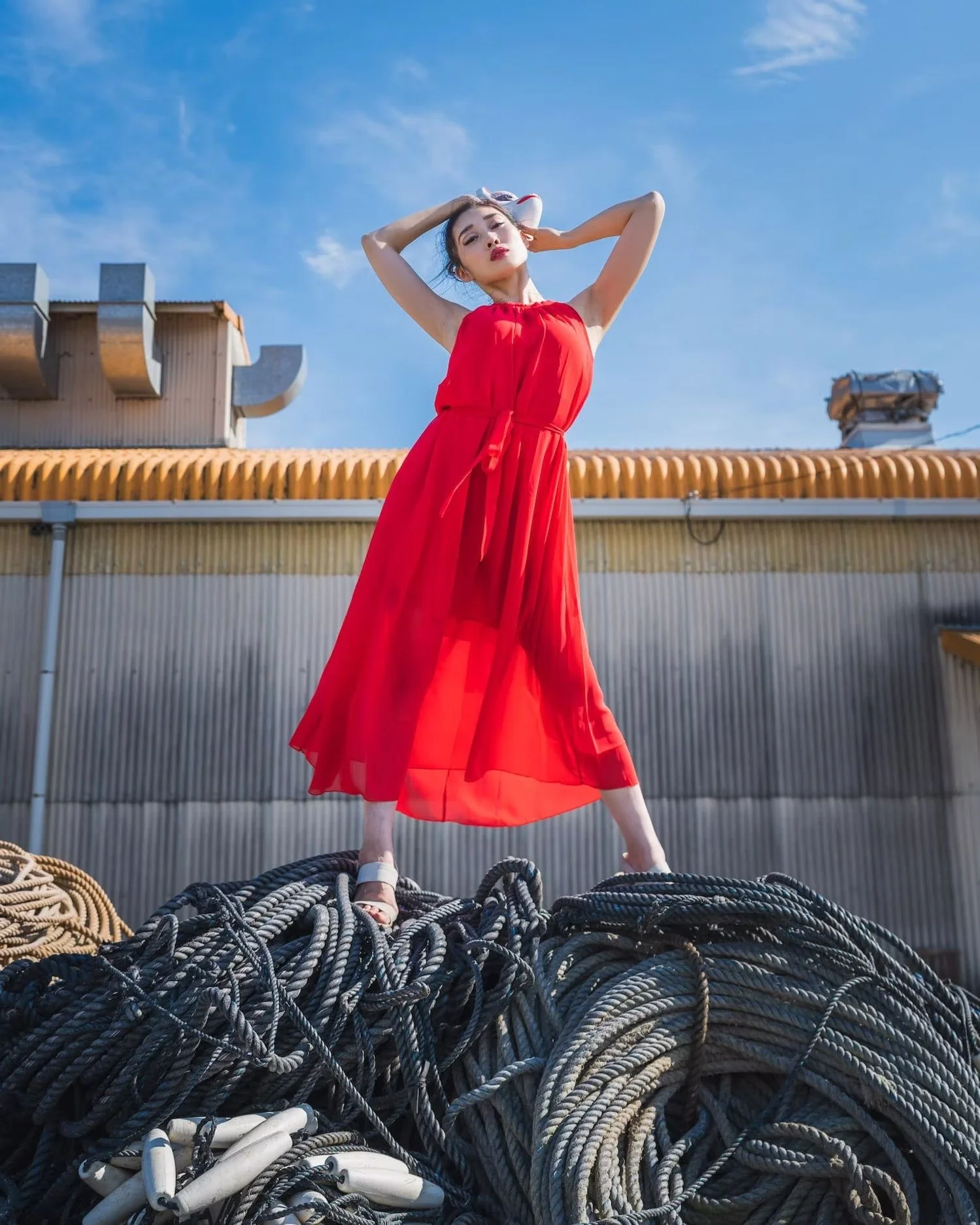 A woman in a red dress posing atop a pile of tangled ropes outdoors against a blue sky.