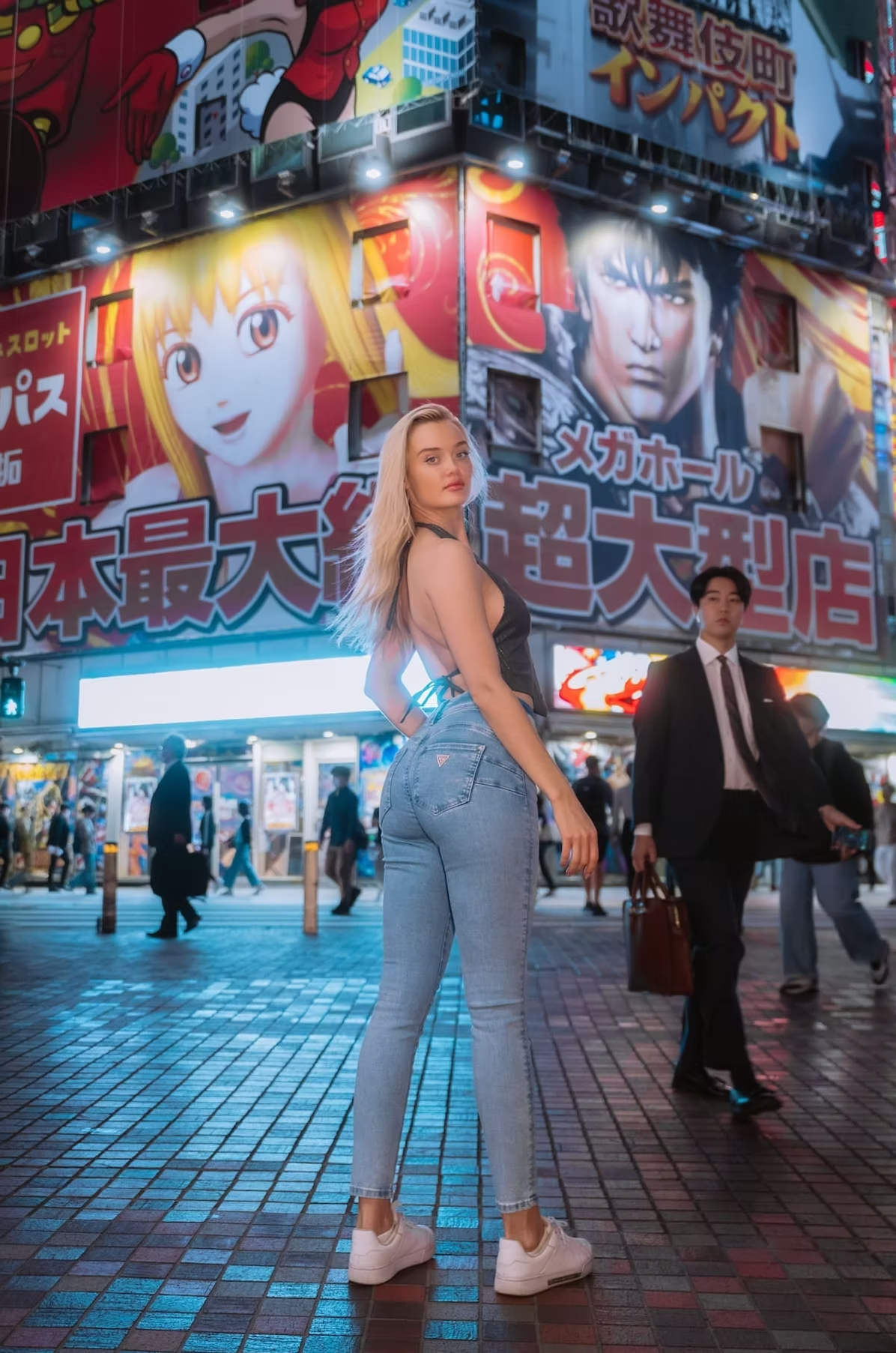 A woman wearing a white top and blue jeans poses on a busy Tokyo street with large neon advertisements and billboards in the background.
