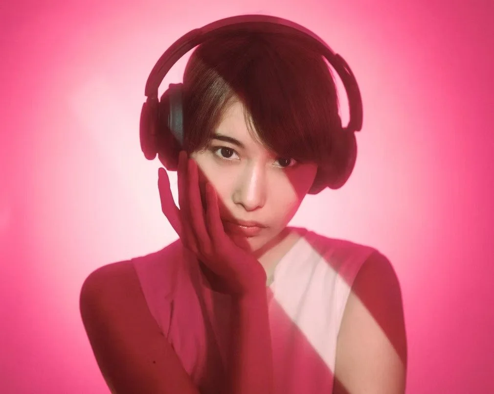 A woman with bold red lighting and headphones gives a mysterious and seductive gaze, exuding a modern, confident vibe in the striking contrast of the neon colors.