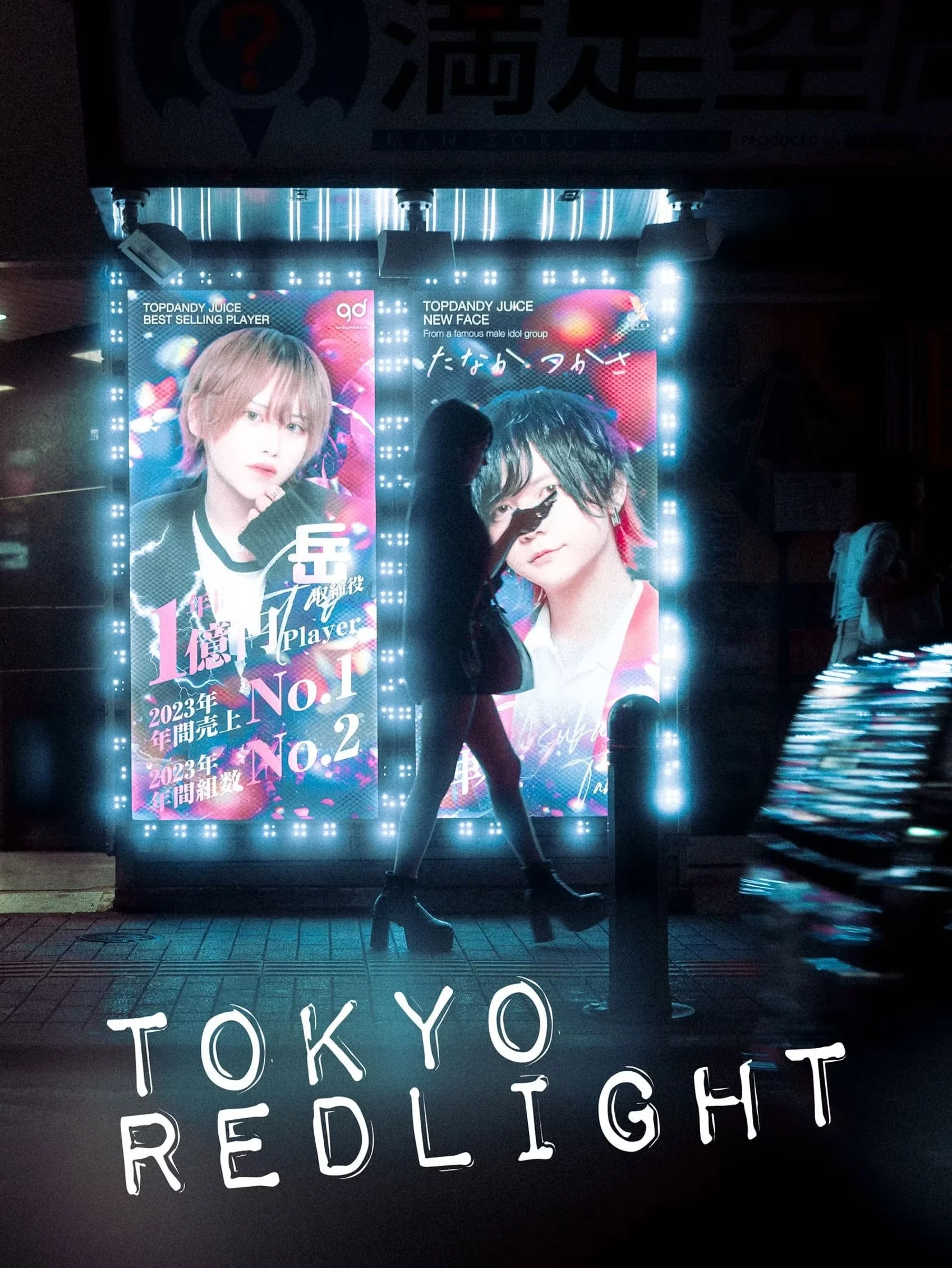 Brightly lit billboard in Tokyo featuring two young male models, with text in Japanese and English promoting a music group or album.