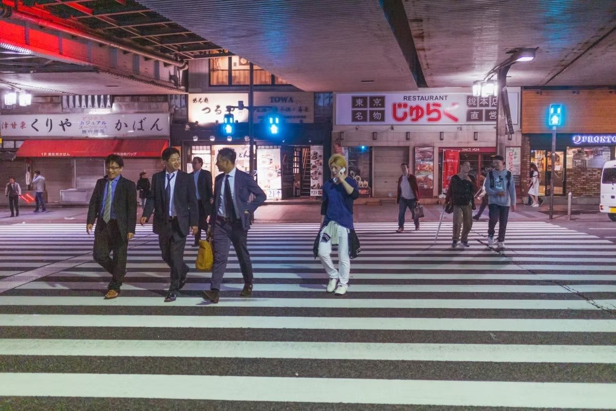 People crossing a crosswalk at night with illuminated signs and store signs in the background in Japan in Shibuya at night.