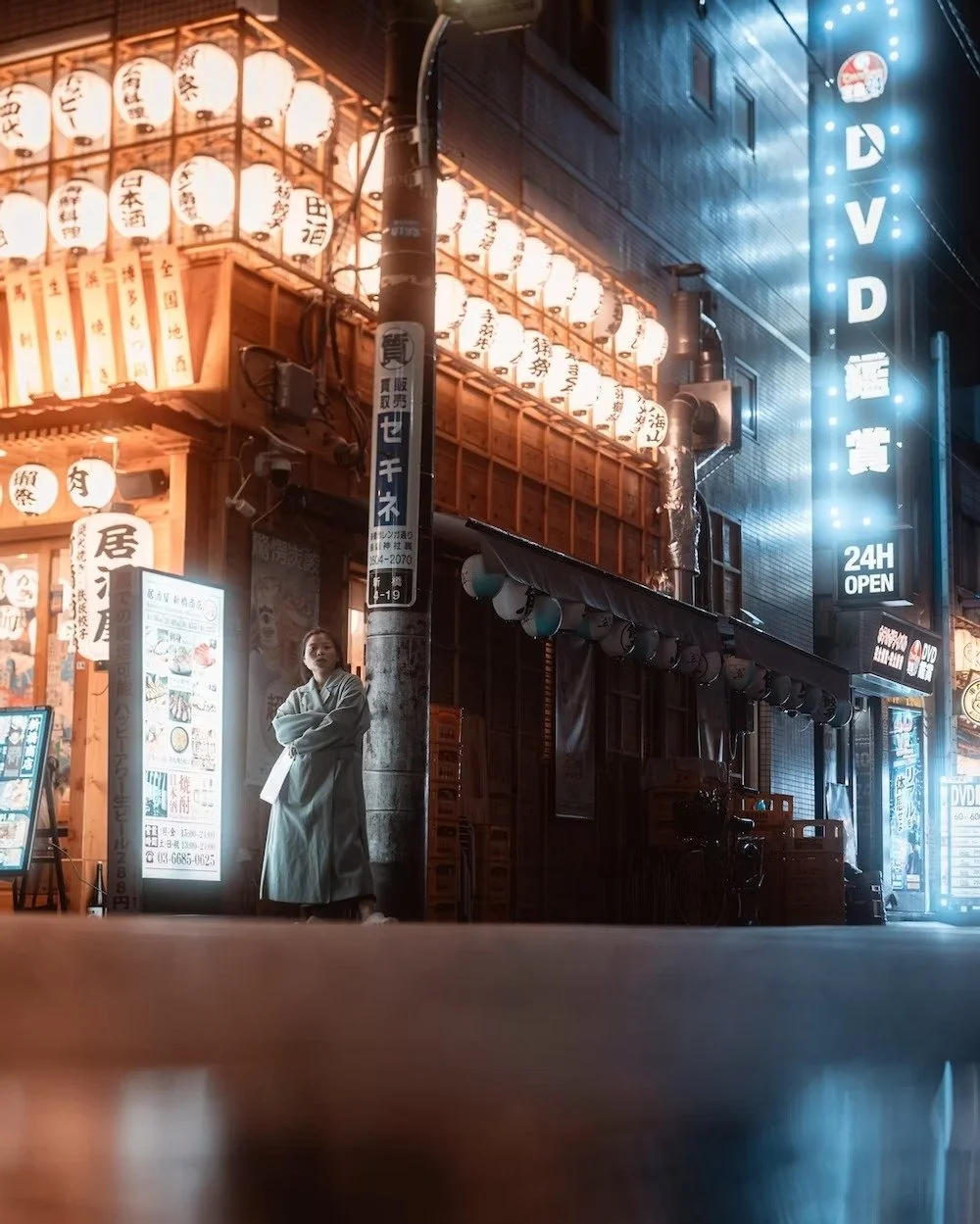 Night street scene in Shimbashi Tokyo, with illuminated paper lanterns and neon signs, a woman in traditional attire standing outside a restaurant.