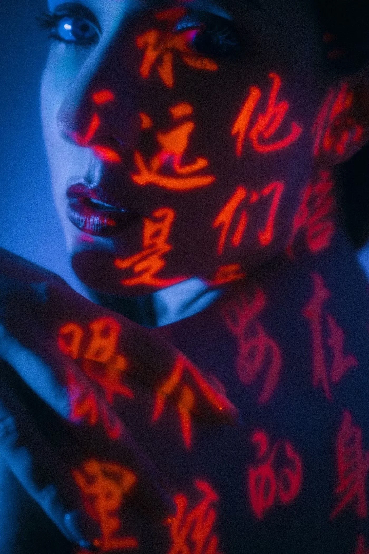 A woman's face partially illuminated with red script text projected onto her face, with blue lighting on the other side.