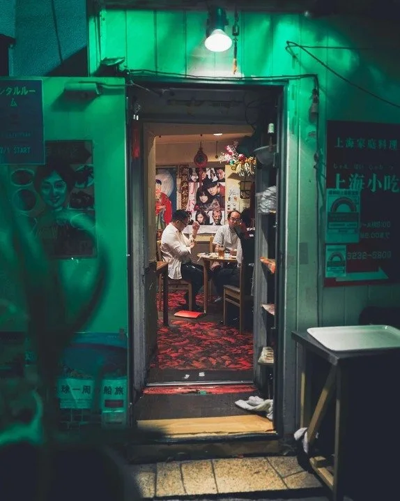 A view through a doorway in Kabukicho, showing two people dining under green neon lights.