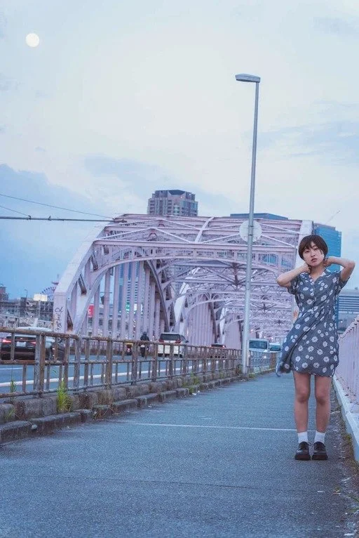 A girl in a blue dress standing on a bridge with the Osaka skyline behind her, capturing the city’s atmosphere.