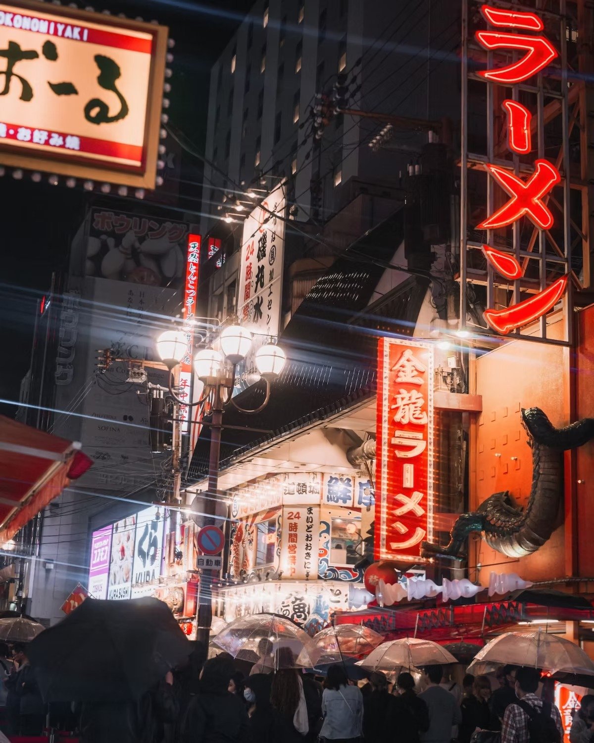 A busy street scene in Japan at night with neon signs, street lamps, and a crowd holding umbrellas in Osaka Dotonbori.