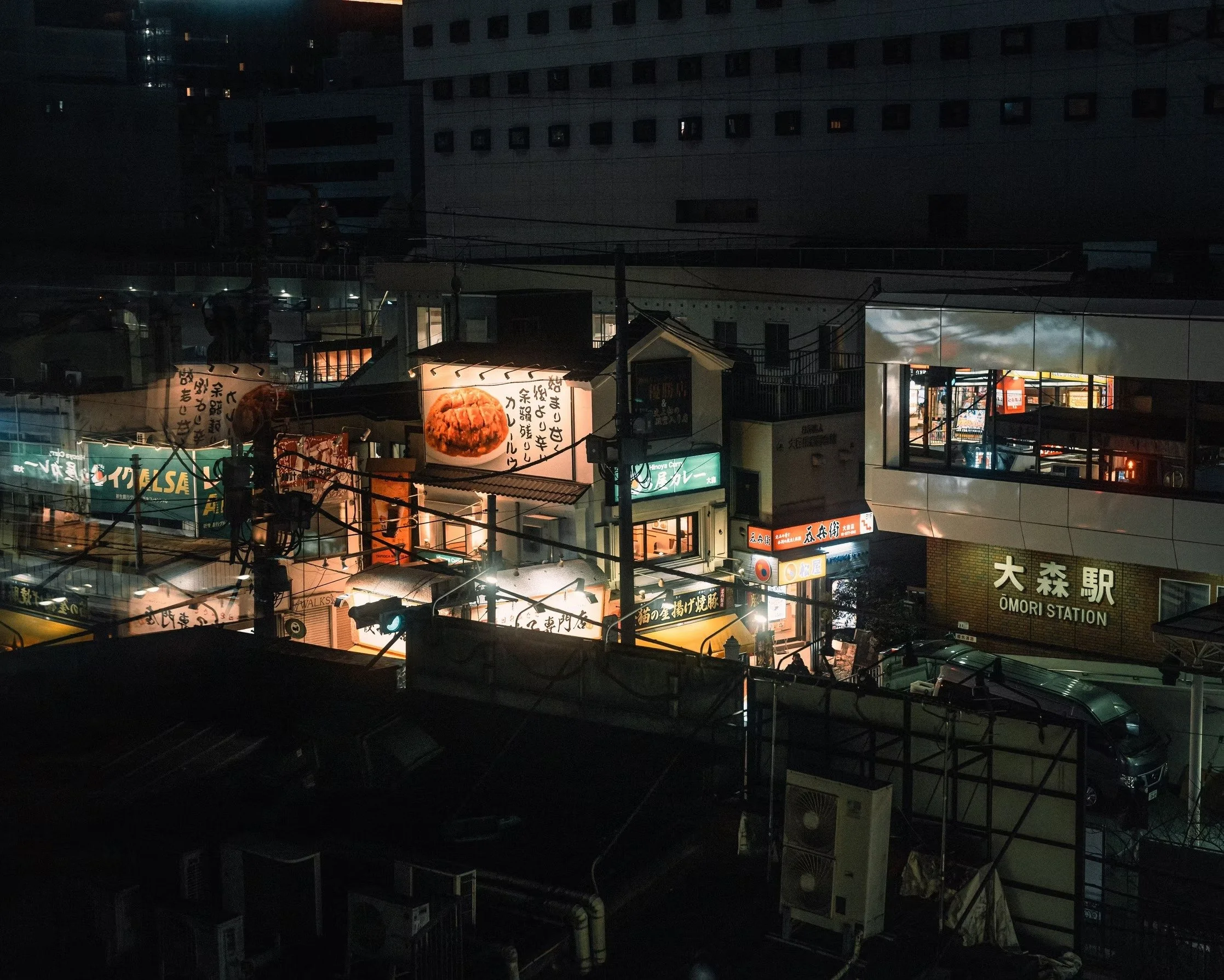 Nighttime city scene with illuminated supermarket signs, buildings, and power lines.
