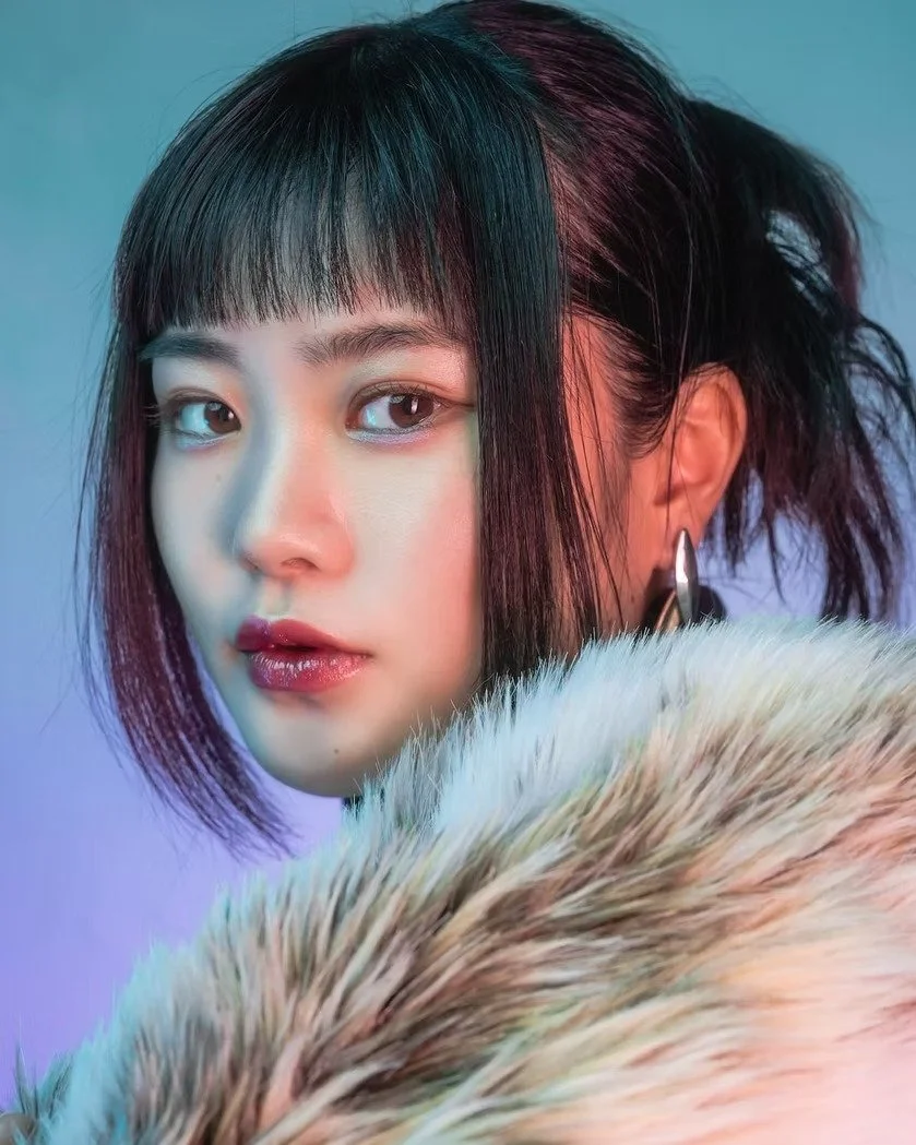 A woman in a fur-trimmed coat gazes intensely at the camera. The cool-toned lighting and soft textures create a fashionable winter-themed aesthetic.