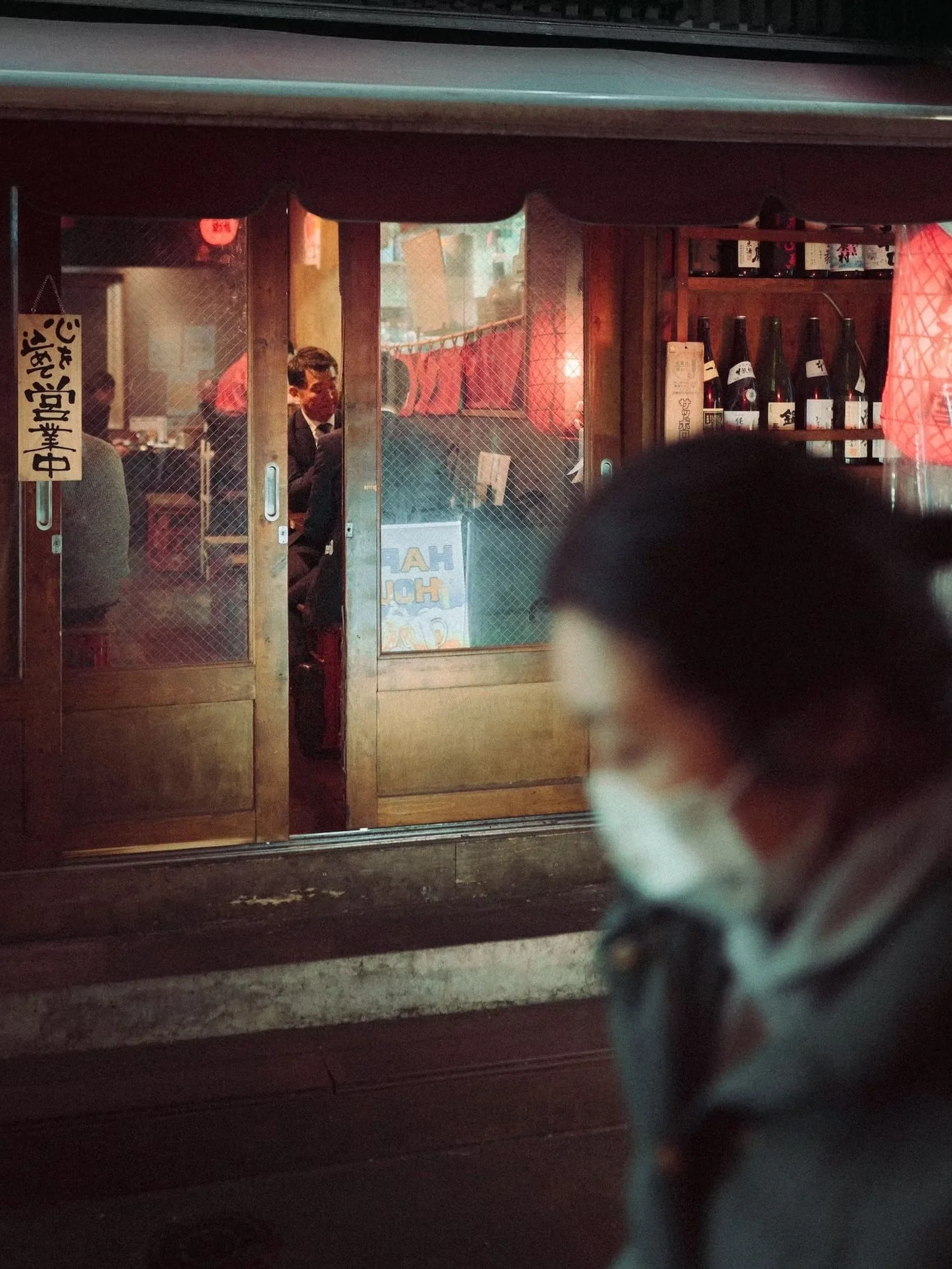 A view through a restaurant or bar window showing customers seated inside, with a dog in the foreground partially obstructing the view. The dog is looking in the direction of the window.