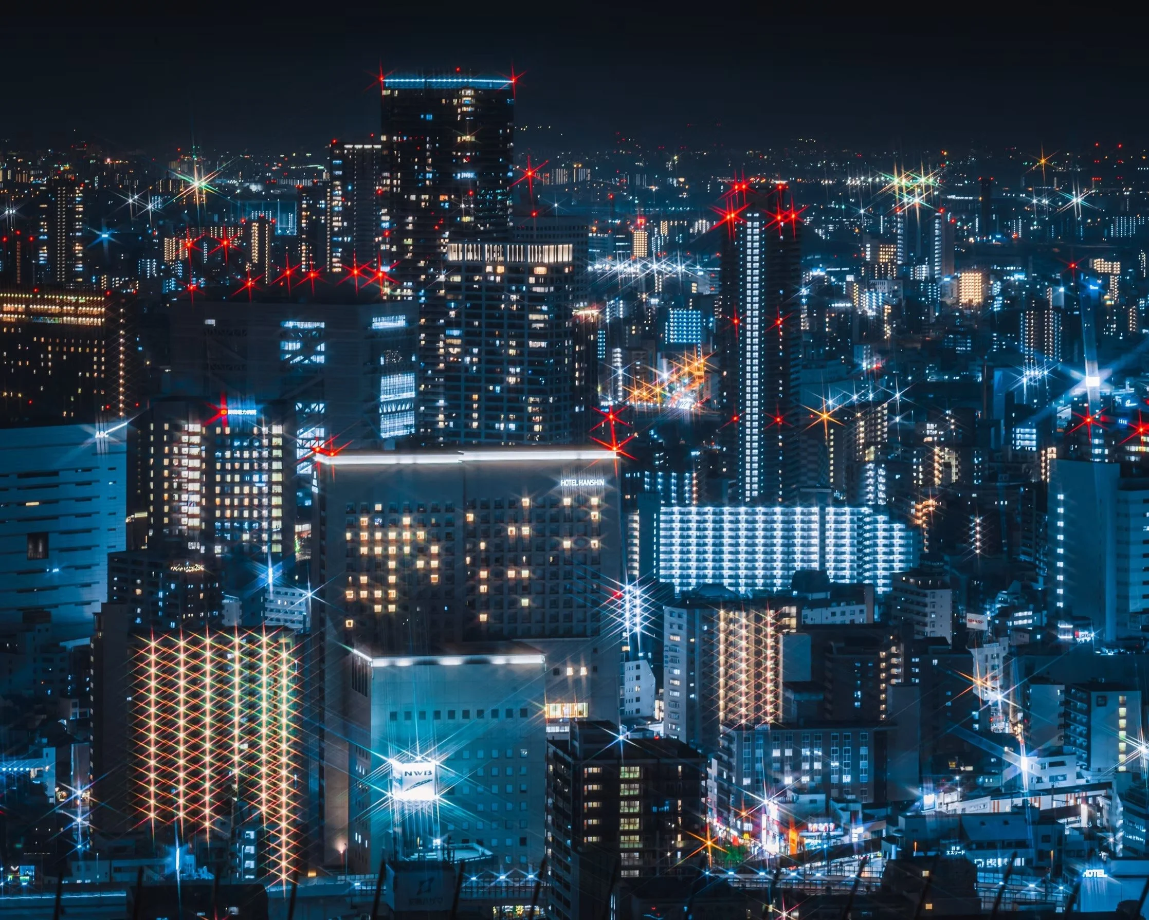 Nighttime cityscape of Osaka Japan view of illuminated skyscrapers and buildings with bright lights and starburst effect across the skyline.