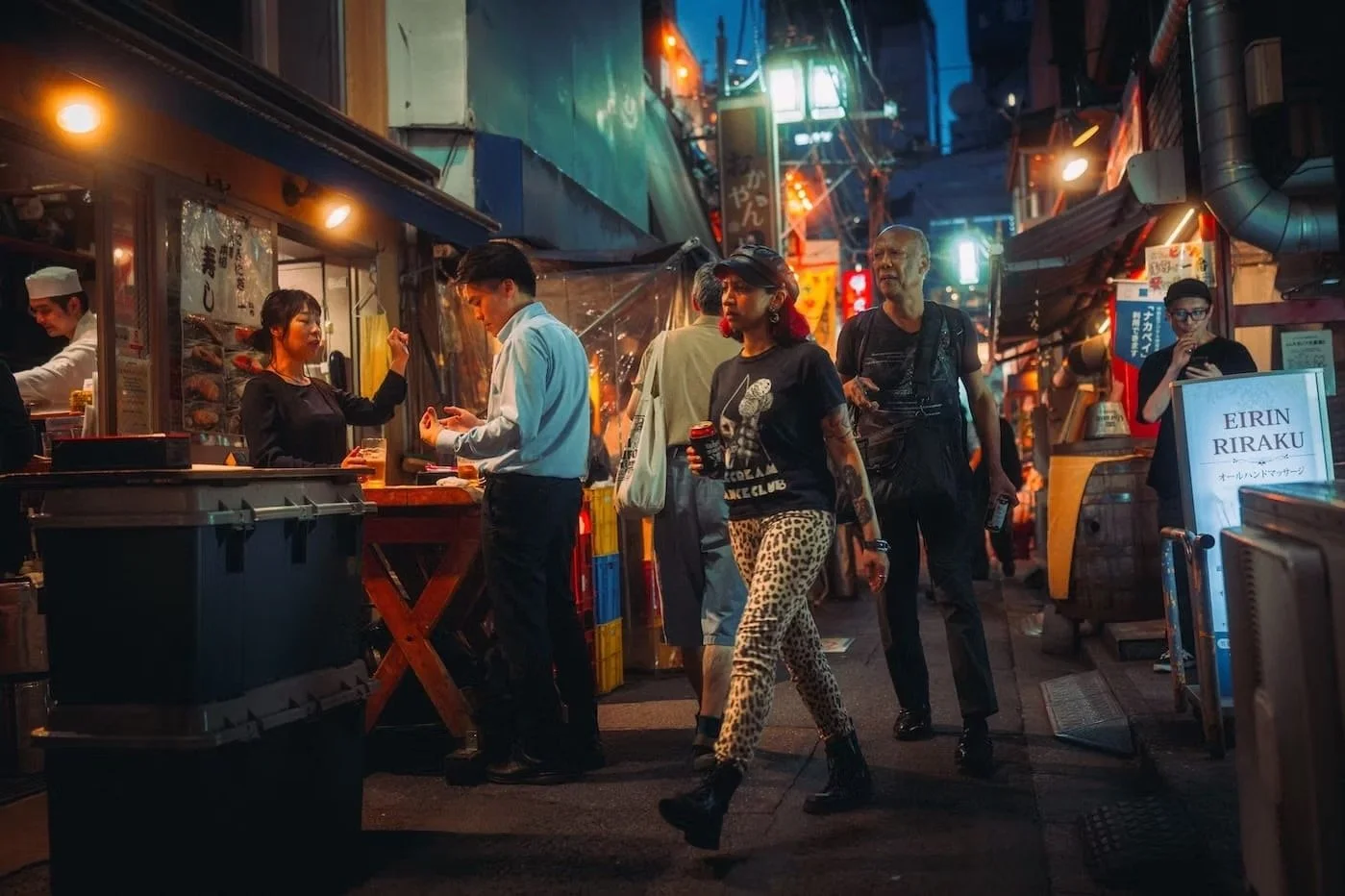 Night street scene with people walking past food stalls and shops, illuminated by colorful neon lights. Nakano night scenes in Tokyo.