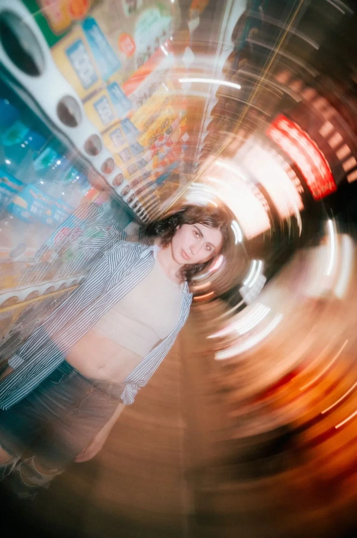 A woman stands calmly on a bustling Tokyo street, surrounded by swirling motion blur of city lights and colors. The dynamic effect captures the energy of the urban environment. Street photography by Deniz Demir.