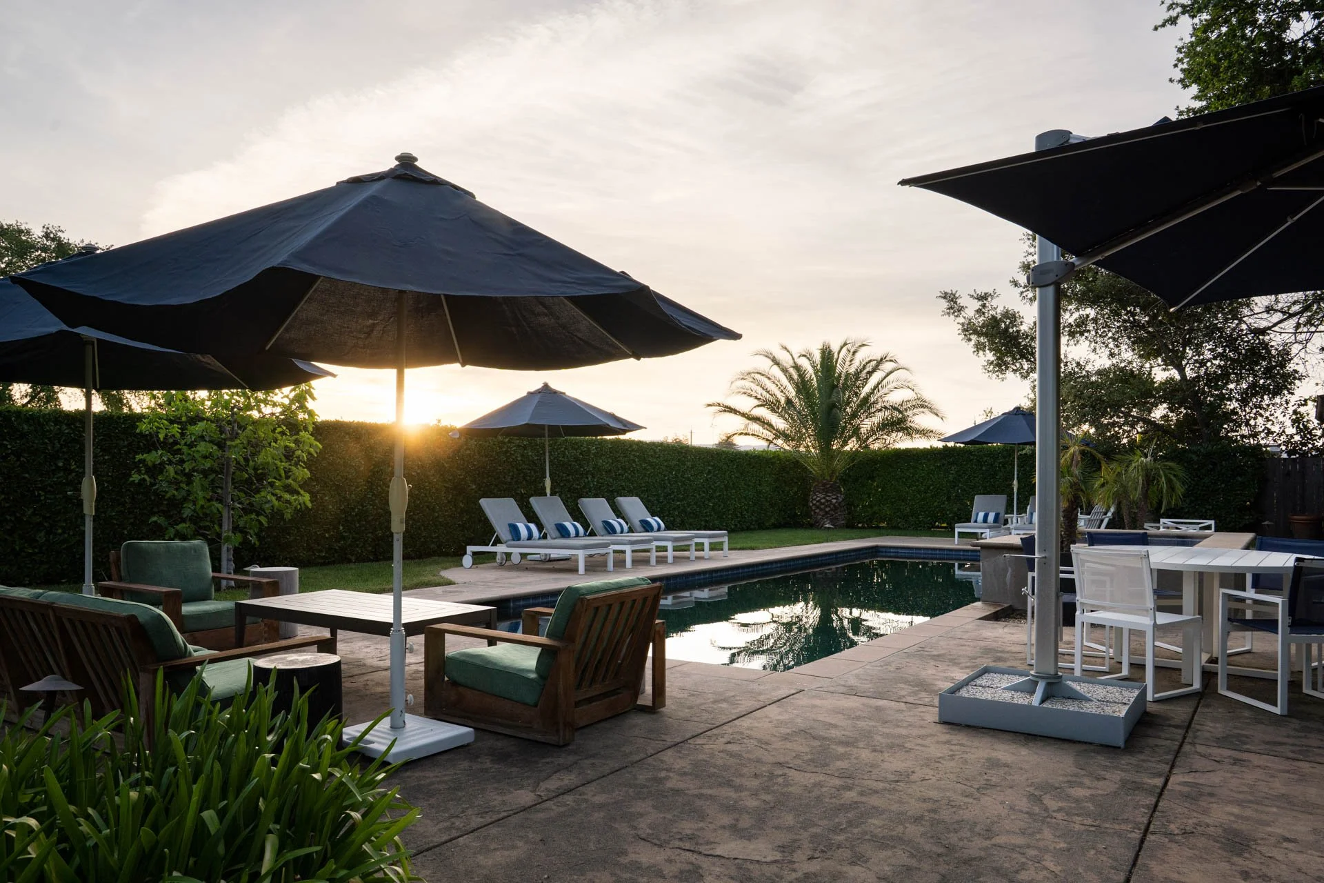 Poolside patio with lounge chairs, umbrellas, and outdoor furniture at sunset