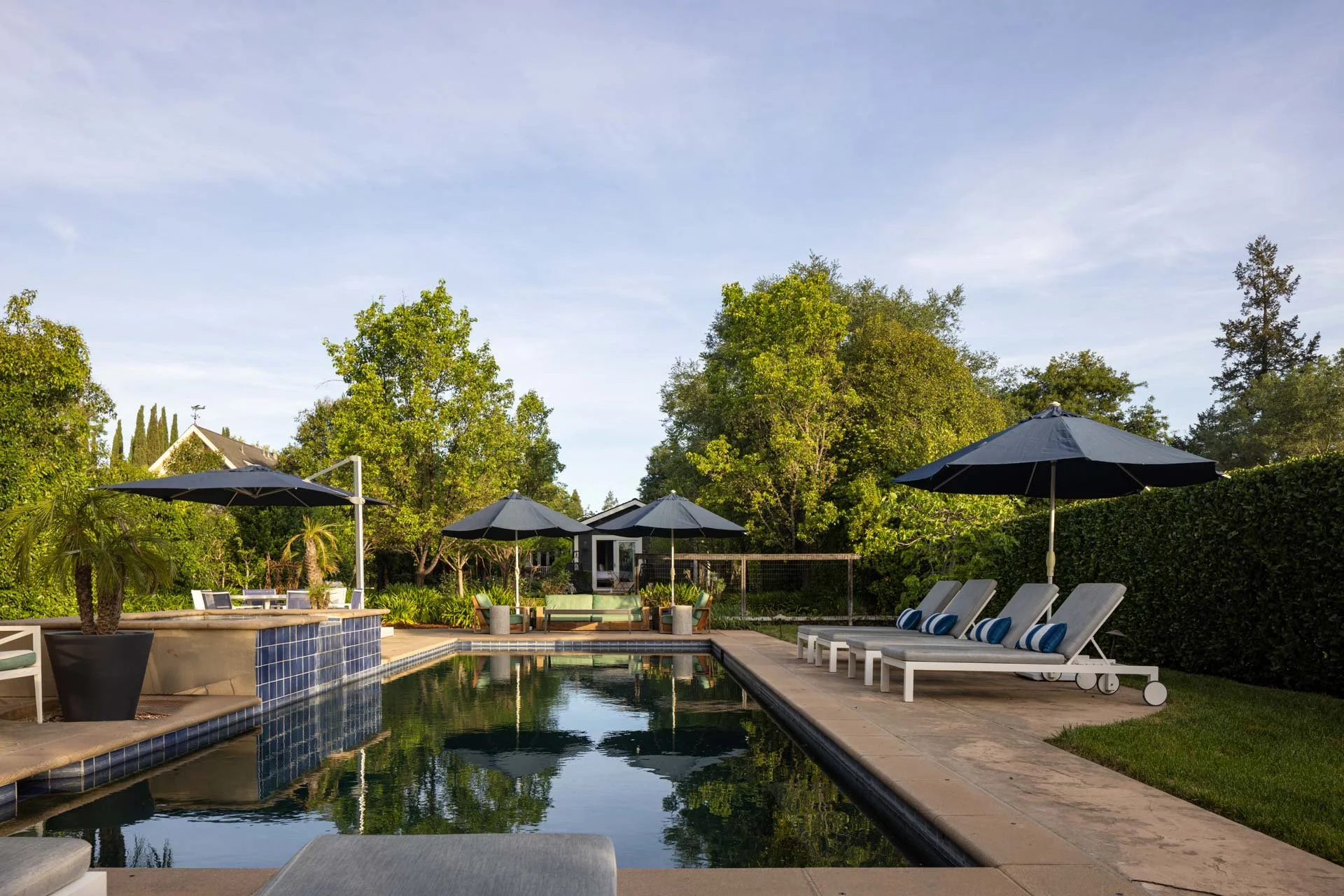 Backyard swimming pool with lounge chairs, umbrellas, and lush greenery.