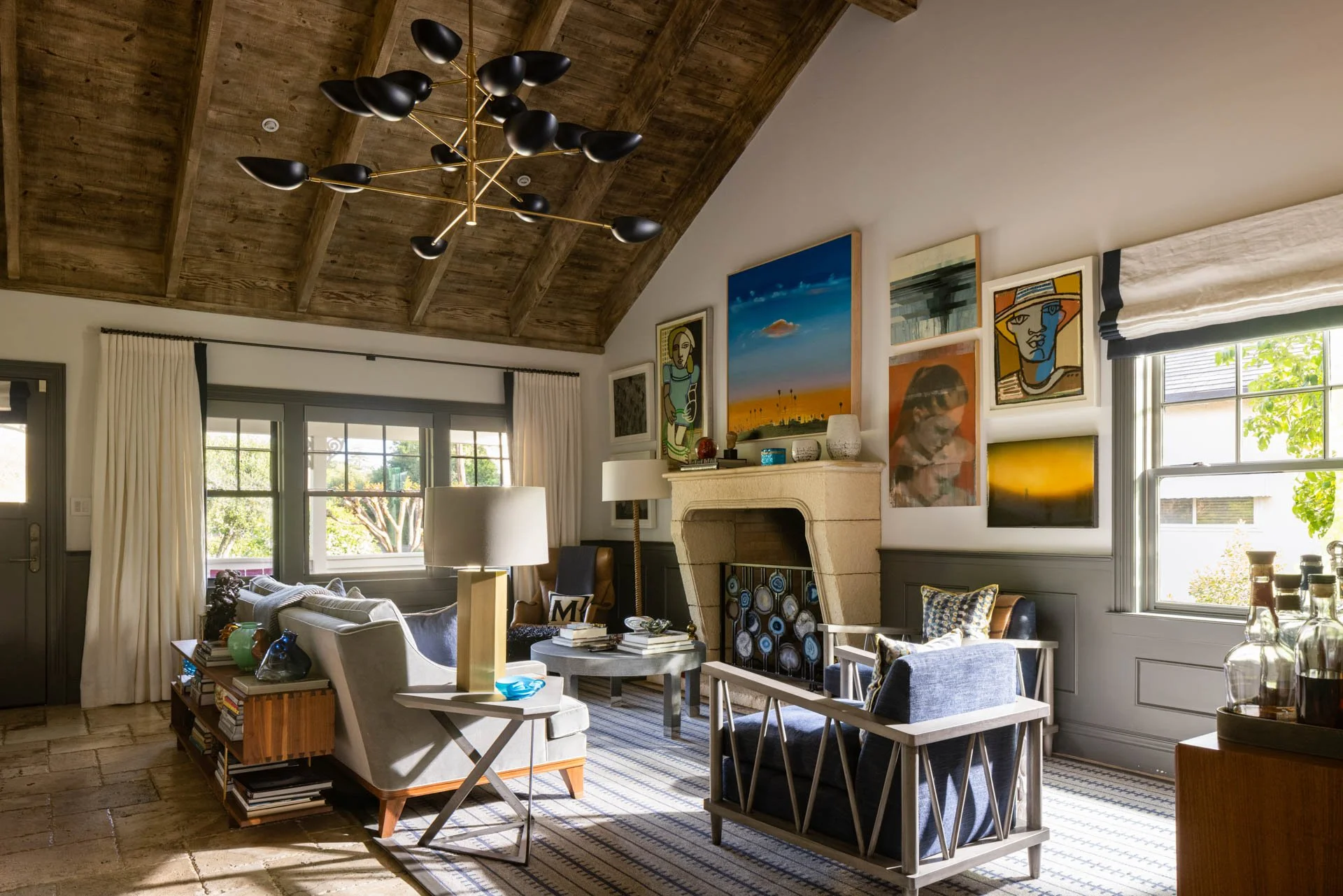Living room with stone fireplace, colorful artwork on wall, large windows, and modern furniture.