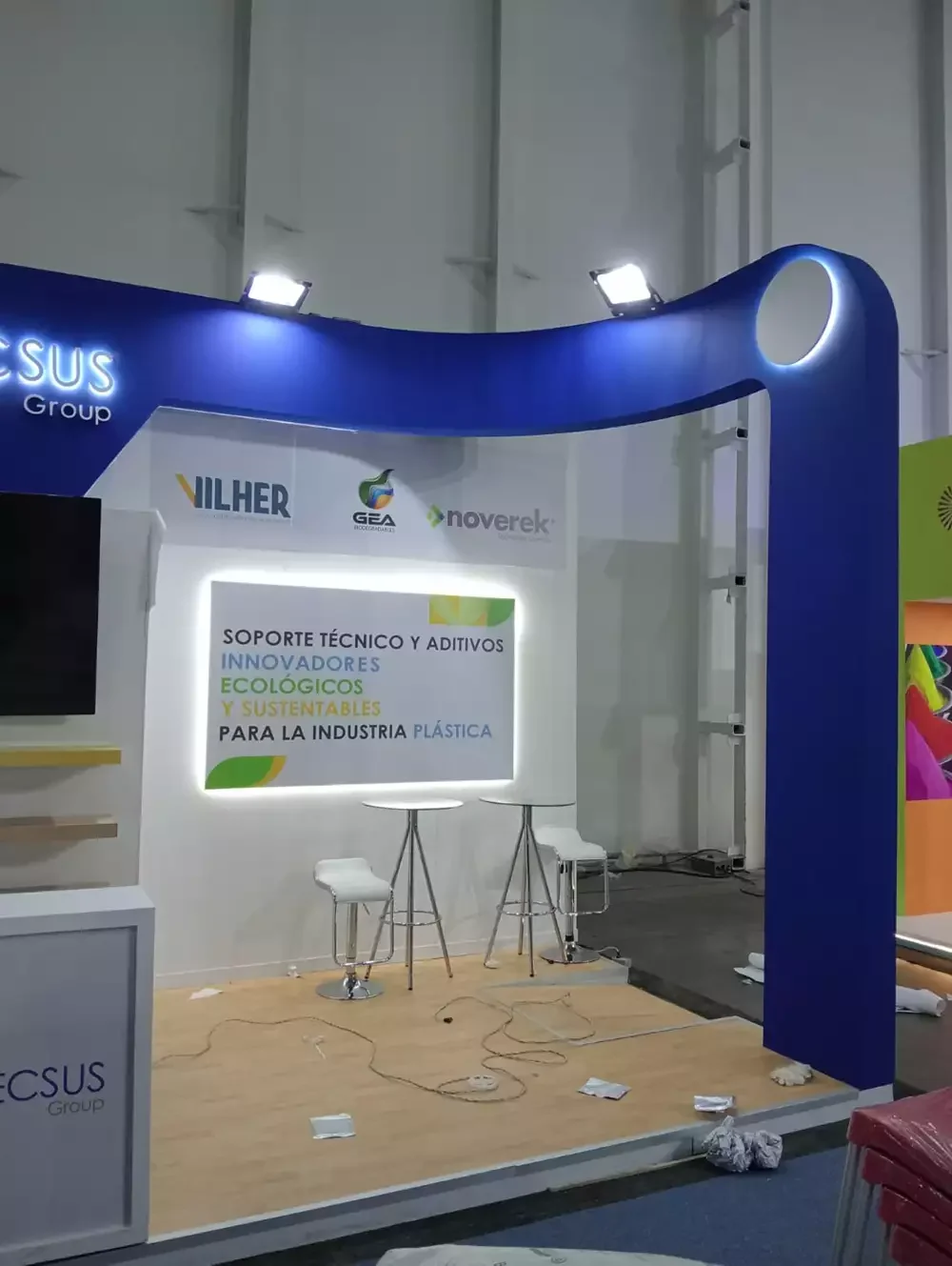 Stand con arco estructural azul y área de mesas para asesoría técnica en plásticos ecológicos.