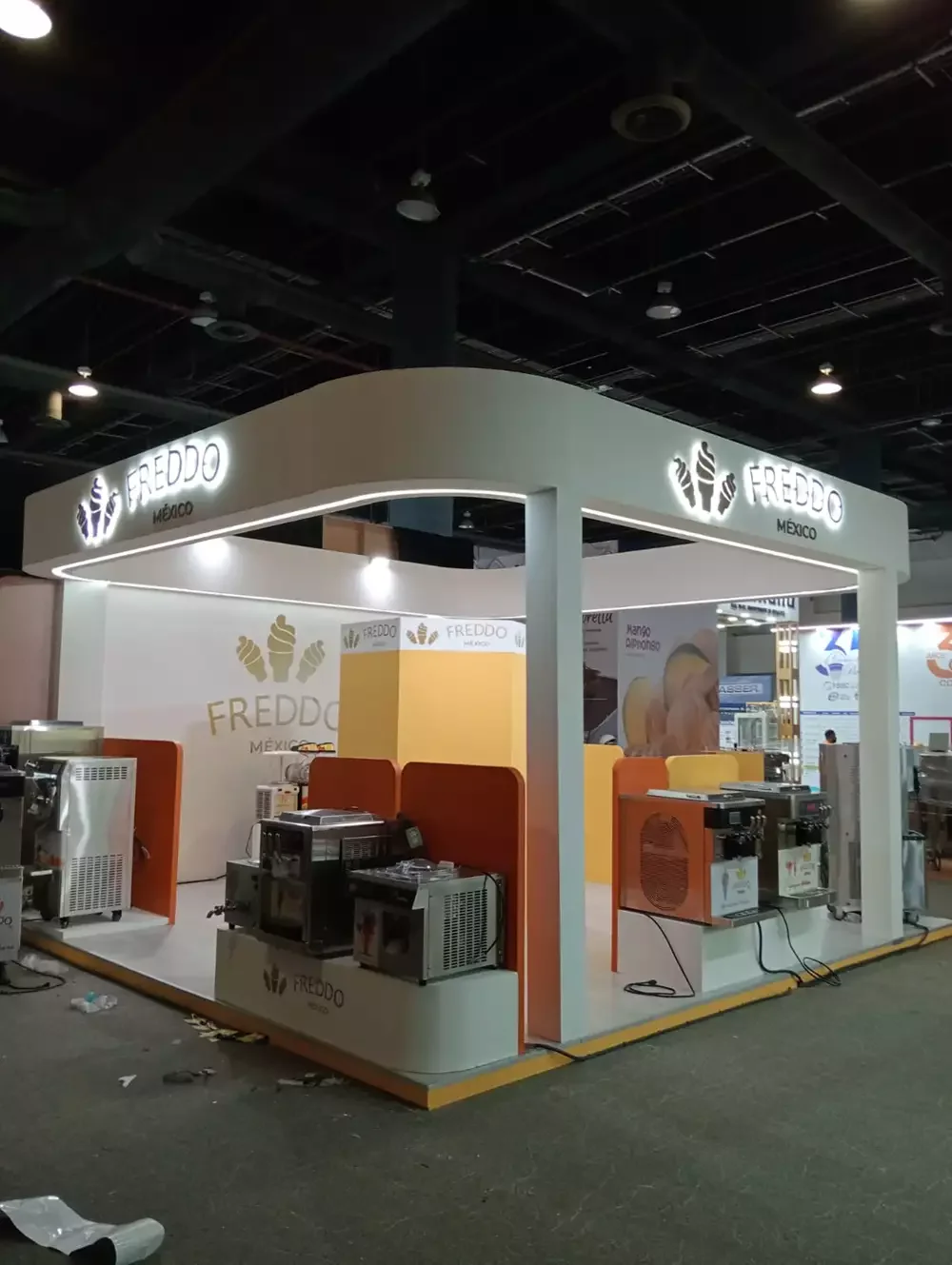Configuración de stand para marcas de consumo con exhibición de equipos automáticos y logos retroiluminados.