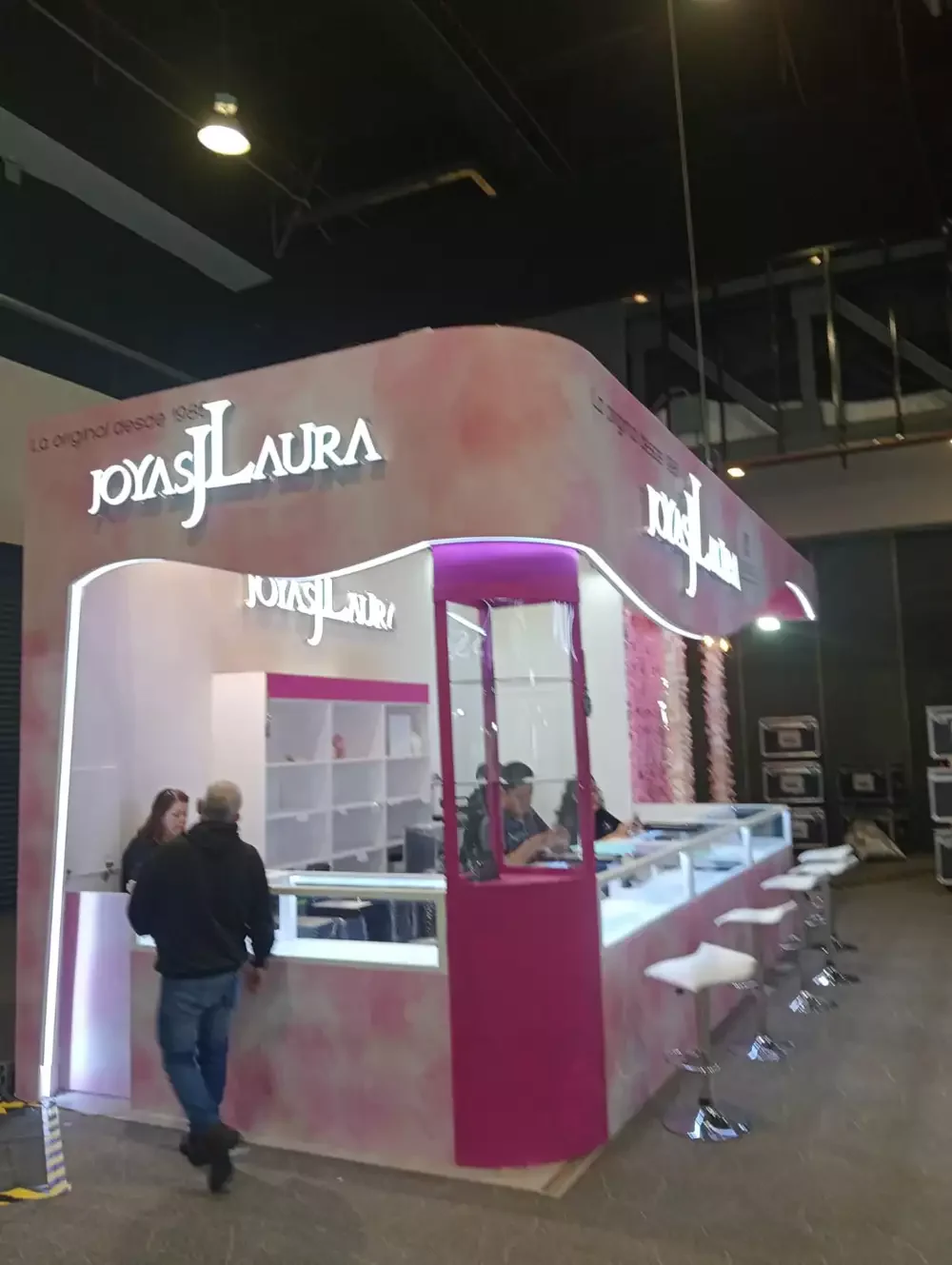 Stand premium con acabados en rosa y blanco, mostrador con bancos y señalética luminosa de alto impacto.