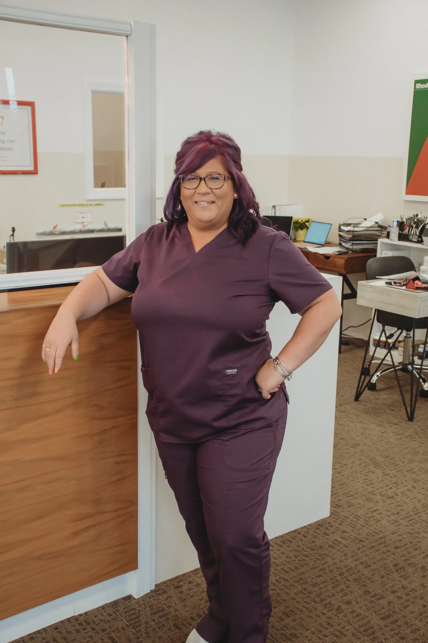 A woman with purple hair and glasses standing in the optometrist office lobby in North Kingstown RI