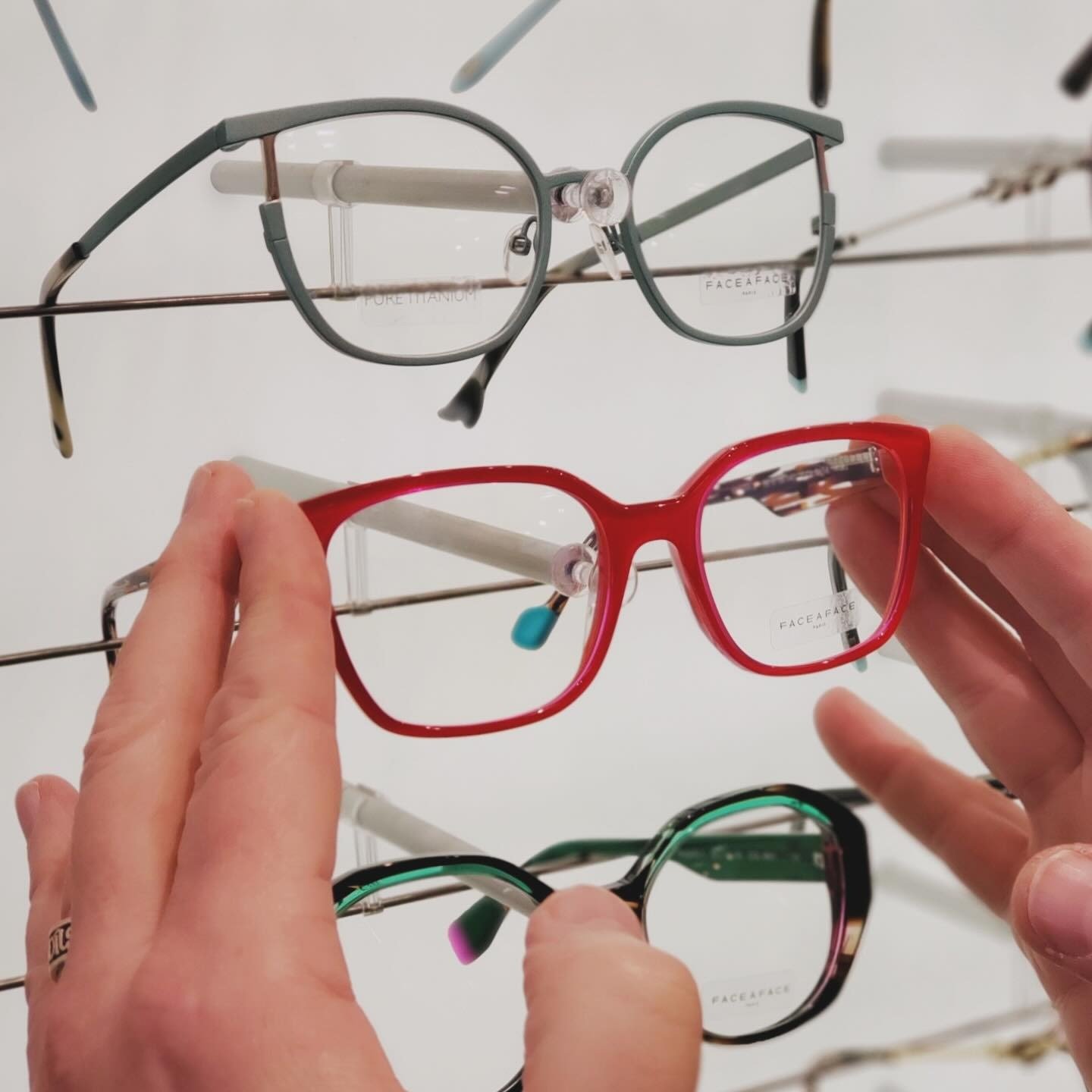 Person inspecting a red pair of eyeglasses among other colorful eyeglasses on display.
