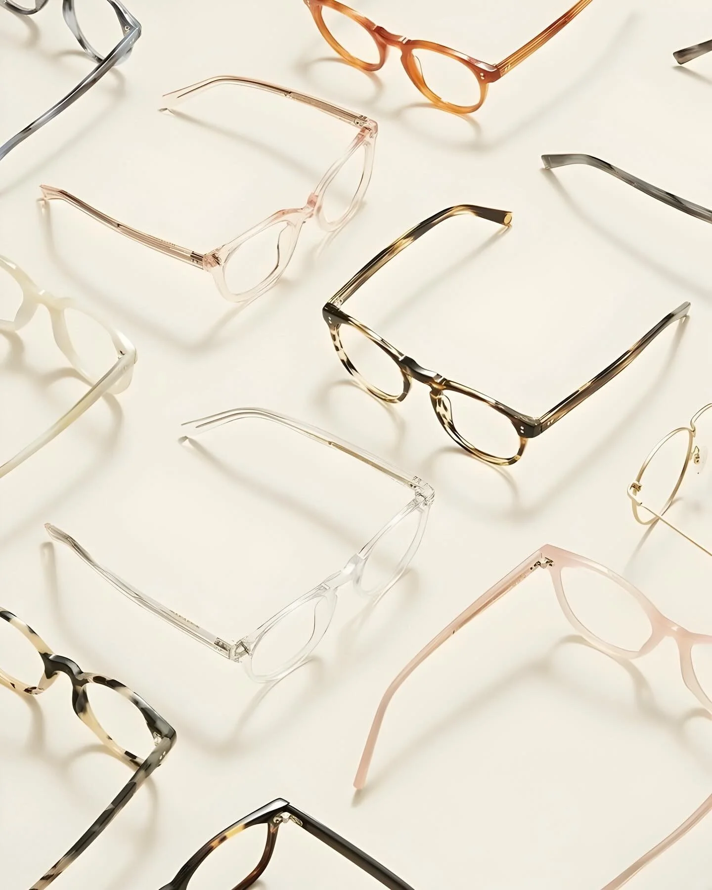 Several pairs of eyeglasses with different frame styles and colors are scattered on a white surface.