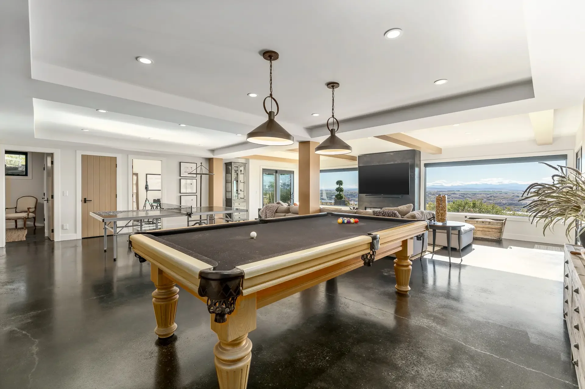 Spacious living room with a pool table, television, large windows showing an outdoor view, and modern decor.