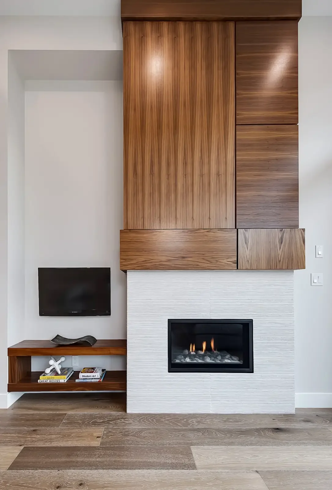 Modern living room with white walls, a black fireplace inset into a white textured wall, a small mounted flat-screen TV, and wooden cabinetry with varied tones and grain patterns above the fireplace and on a low shelf.